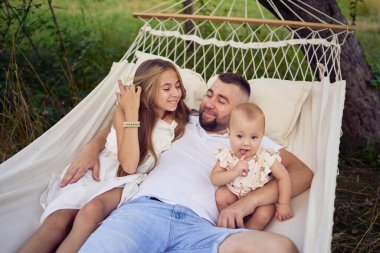 Baba kızlarıyla oynuyor, bir bebek ve bir hamakta genç kız.