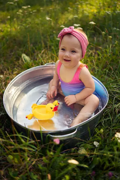 stock image a baby in a metal tub plays with rubber ducklings in the summer garden