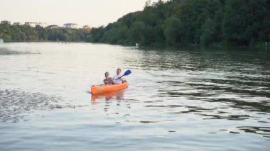 Birbirlerine aşık çiftler gün batımında nehirde kano yapıyorlar.