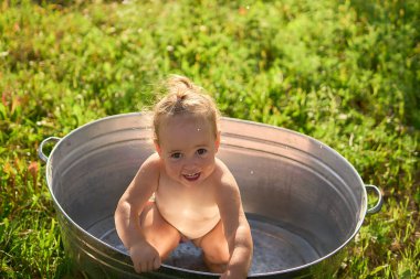 Bir çocuk sıcak bir günde bahçedeki küvette su sıçratır ve oynar.             