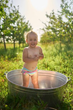 Bir çocuk sıcak bir günde bahçedeki küvette su sıçratır ve oynar.             