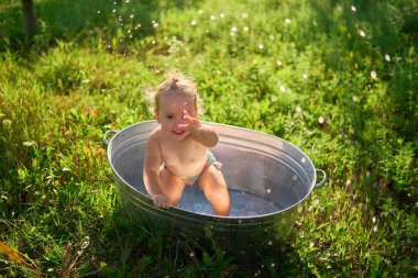 Bir çocuk sıcak bir günde bahçedeki küvette su sıçratır ve oynar.             