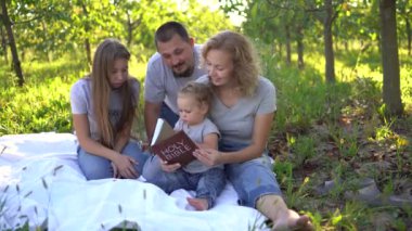 Bahçedeki piknikte İncil okuyan bir aile.