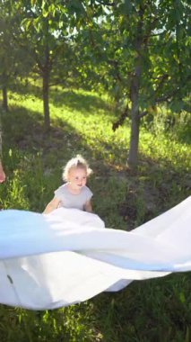 Dört kişilik bir aile bahçede beyaz bir çarşafla oynuyor. Bir çocuk çarşafı sallamak istiyor.