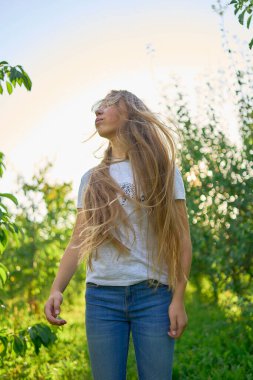 Güneşli bir bahçede uzun sarı saçlı genç bir kızın portresi.