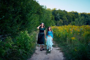 Yazın gün batımında bir tarlada tuhaf bir estetik elbise giymiş iki kadın.