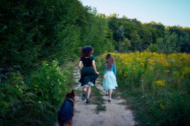 Yazın gün batımında bir tarlada Alman bir çobanla garip bir estetik elbise giymiş iki kadın.