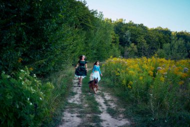 Yazın gün batımında bir tarlada Alman bir çobanla garip bir estetik elbise giymiş iki kadın.