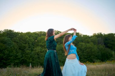 Yazın gün batımında bir tarlada dans eden tuhaf estetik stil elbiseli iki kadın.