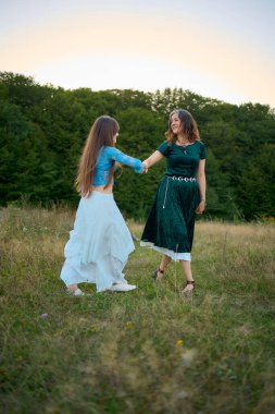Yazın gün batımında bir tarlada dans eden tuhaf estetik stil elbiseli iki kadın.
