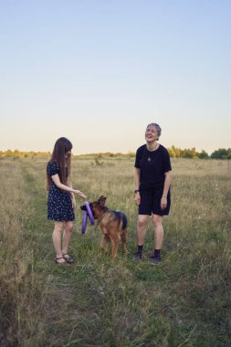 İki kadın gün batımında bir Alman çoban köpeği oyuncağıyla sahada oynuyor.