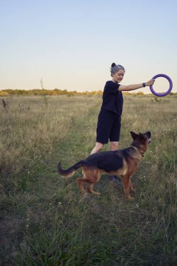İki kadın gün batımında bir Alman çoban köpeği oyuncağıyla sahada oynuyor.