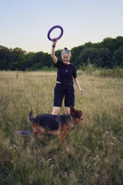 İki kadın gün batımında bir Alman çoban köpeği oyuncağıyla sahada oynuyor.