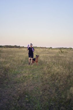 İki kadın gün batımında bir Alman çoban köpeği oyuncağıyla sahada oynuyor.