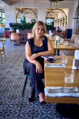               Orta yaşlı ve zengin bir kadın şık bir restoranda eski moda kıyafetler giyiyor.                                                 