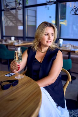 Orta yaşlı ve yaşlı bir kadın. Eski moda kıyafetler içinde. Lüks bir restoranda köpüklü şarap içiyor.                     