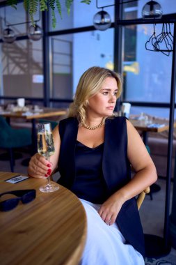 Orta yaşlı ve yaşlı bir kadın. Eski moda kıyafetler içinde. Lüks bir restoranda köpüklü şarap içiyor.                     