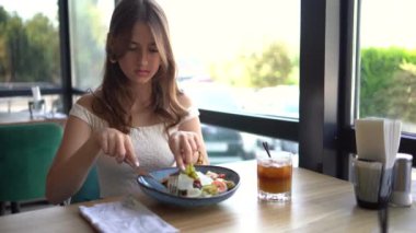 16 yaşında, eski moda elbiseli genç bir kız süslü bir restoranda kahveli salata yiyor.