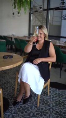 Orta yaşlı ve yaşlı bir kadın. Eski moda kıyafetler içinde. Lüks bir restoranda köpüklü şarap içiyor.