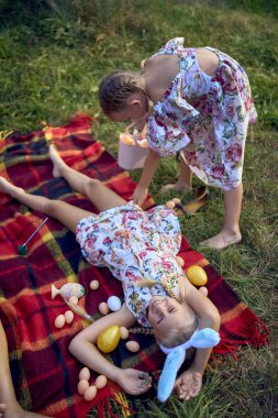 little girls, sisters, playing on a picnic blanket with eggs after  Easter egg hunt clipart