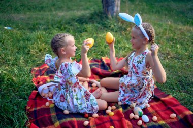 little girls, sisters, playing on a picnic blanket with eggs after  Easter egg hunt clipart