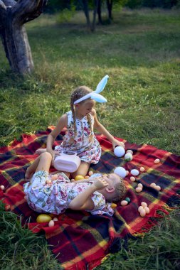 little girls, sisters, playing on a picnic blanket with eggs after  Easter egg hunt clipart