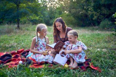 Bir anne ve iki kızı kutsal kitabı okuyup Paskalya pikniğinde dua ediyorlar.