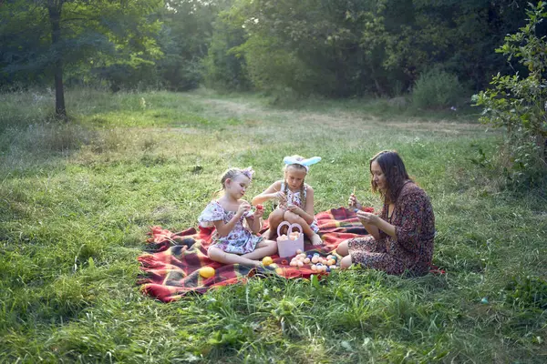 İki küçük kız ve anne Paskalya pikniğinde yumurta boyuyor.