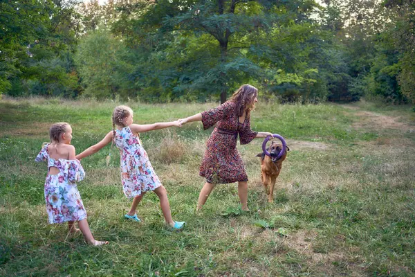            Anne ve küçük kız kardeşler bahçede Paskalya pikniğinde Alman çoban köpeğiyle oynuyorlar.                    