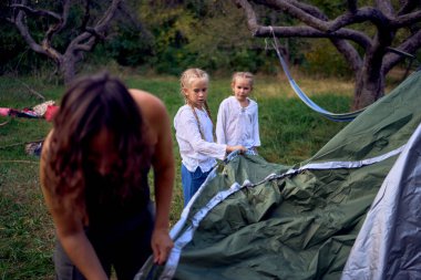               Anne ve küçük kızları ormanda bir çadır kuruyorlar, çocuklarla kamp yapıyorlar.                                                