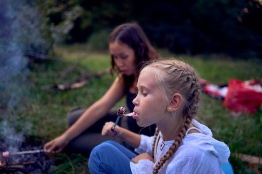 Anne ve kızları kamp ateşinde kızartıp marshmallow yiyorlar, çocuklarla kamp yapıyorlar.