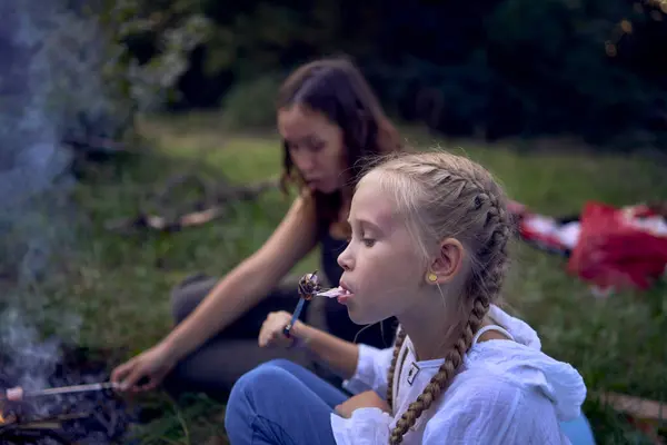 stock image mother and her daughters  roasting and eating marshmallows on the campfire, camping vacation with children