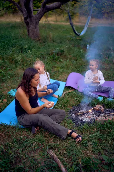 stock image mother and her daughters  roasting and eating marshmallows on the campfire, camping vacation with children