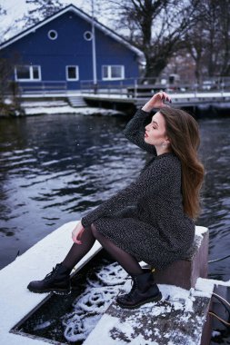 Uzun sarı saçlı, güzel bir kadın. Açık renk bir elbise giymiş. Kış gölünün iskelede kar altında.                       