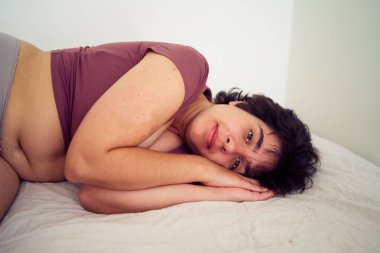 Oyuncu bir genç kadın, öğrenci yurdunda yatağında ev kıyafetleri içinde.