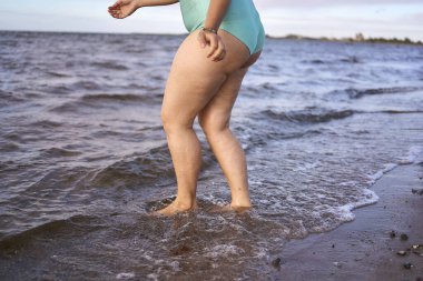  a young plus-size woman is engaged in winter swimming and warming up by the sea                     clipart