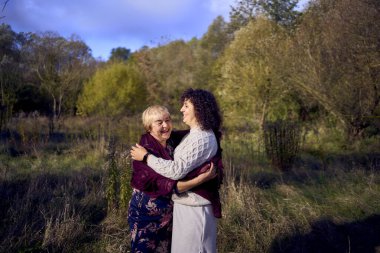 Orta yaşlı bir kız ve yaşlı bir anne birlikte sonbahar ormanında yürüyüş yapıyorlar.                   