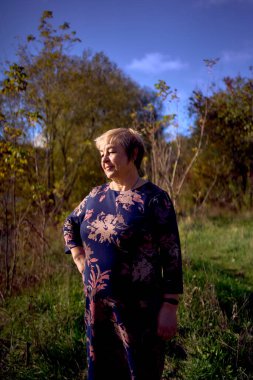 Sonbahar ormanında gri saçlı, elbisesi olan yaşlı bir kadının portresi.                                                    