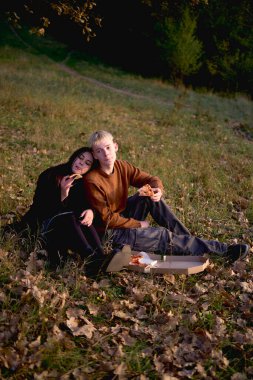       15 yaşındaki aşık genç bir çift sonbahar parkında piknik yaparken pizza yiyor.                         