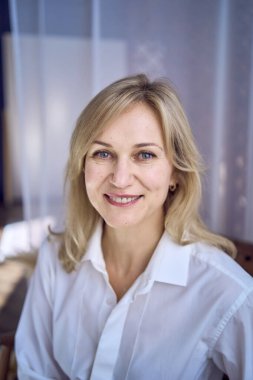 Beyaz bluz ve bej pantolon giymiş orta yaşlı şık bir kadının portresi.                    