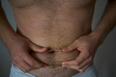  30 yaşında orta yapılı bir adam elleriyle deri ve yağ kıvrımlarını ovuyor.                          