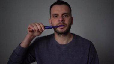 30 yaşındaki bir adam elektrikli diş fırçası kullanarak dişlerini mor diş macunuyla fırçalıyor.