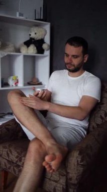 30 yaşındaki bir adam bacaklarının derisine nemlendirici krem sürüyor.