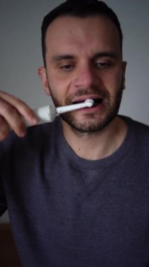 30 yaşındaki bir adam elektrikli diş fırçası kullanarak dişlerini mor diş macunuyla fırçalıyor.