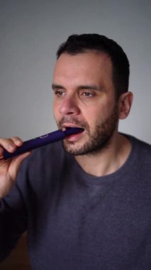 30 yaşındaki bir adam elektrikli diş fırçası kullanarak dişlerini kömür diş macunuyla fırçalıyor.