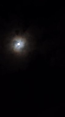 Gece gökyüzünde dolunay var. Fenerlerle aydınlatılmış gökdelenlerin üstünde.