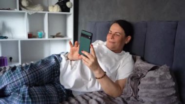 Son sınıf öğrencisi kadın yatakta telefonla konuşuyor.