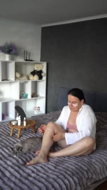 Yatakta iç çamaşırlı yaşlı bir kadın vücut kozmetikleriyle rutin bir kişisel bakım yapıyor.