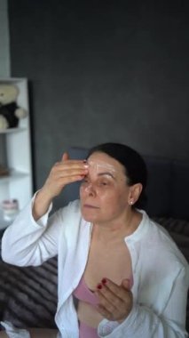 Yatakta iç çamaşırlı yaşlı bir kadın yüz ve vücut estetiğiyle rutin bir kişisel bakım sergiliyor.