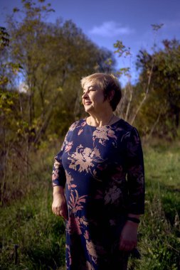 Sonbahar ormanında gri saçlı, elbisesi olan yaşlı bir kadının portresi.                                                    